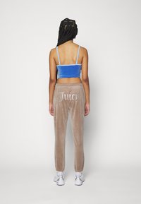Velvet blauwe crop top met dunne bandjes en beige velvet broek met 'Juicy' in rhinestones op de achterkant. Witte sneakers met zilveren accenten.