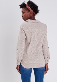 Blusa ligera con un diseño estampado en tonos neutros, que presenta un cuello puntiagudo, puños con botón y un dobladillo redondeado.