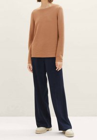 Pull marron côtelé à manches longues, col rond ; associé à un pantalon ample bleu marine foncé et des chaussures de couleur claire. Design simple et texturé.