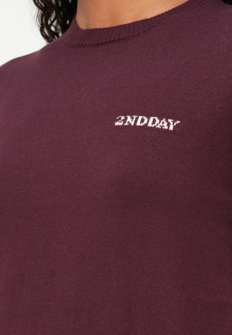 Bordeaux gebreide trui met een ronde halslijn en de tekst "2ND DAY" in het wit geborduurd op de borst. Zachte stoftextuur.