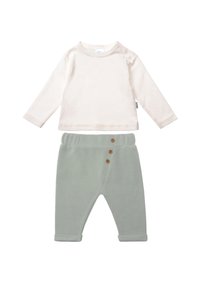 Helles, beiges Langarmshirt mit rundem Halsausschnitt und Schulterknopf, kombiniert mit grünen Hosen, die drei Holzknöpfe und Knöchelabschlüsse haben.