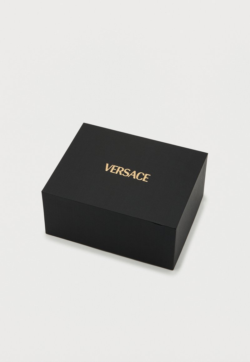 Zwarte rechthoekige doos met een getextureerd oppervlak, met het woord "VERSACE" in goudkleurige, geperste letters op de bovenkant.