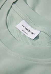 Vihreä rento t-paita, jossa on ribbireunus ja teksturoitu kangas. Tagi lukee "LINDHBERG" ja sen alla on "RELAXED FIT".