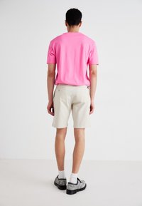 Rožinė marškinėliai trumpomis rankovėmis, smėlio spalvos šortai, pilki tekstūruoti batai. Paprastas dizainas, kasdienis stilius, šviesėjanti fonas.