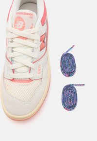 Bijele i ružičaste New Balance 550 tenisice izrađene od mrežastog, suede i gumenog materijala. Uključuju dva role šarenih vezica.