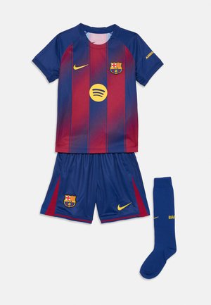 Maillot de football des jeunes du FC Barcelone avec un maillot rayé bleu et rouge, un short bleu et une seule chaussette bleue sur un fond blanc.