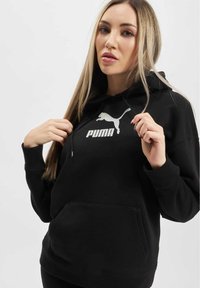 Čierna mikina s kapucňou vyrobená z bavlnenej zmesi, s prednou kengurou vreckom, rebrovanými manžetami a strieborným logom PUMA na hrudníku. Hladká textúra.
