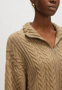 Beige Strickpullover mit hohem Kragen und Reißverschluss, mit strukturierten Musterdetails und langen Ärmeln. Aus weichem Garnmaterial.