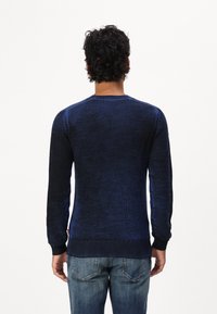 Mörkblå ribbade tröja med långa ärmar, rund hals och strukturerad tyg. Plagget har en mörkare gradiente mot fållen och manschetterna.