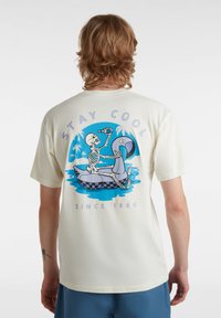 Kurzärmliges, cremefarbenes Baumwoll-T-Shirt mit einem blauen Grafikmotiv eines Skeletts auf einem Schwimmgerät, das von tropischen Akzenten umgeben ist, sowie Text oberhalb und unterhalb.