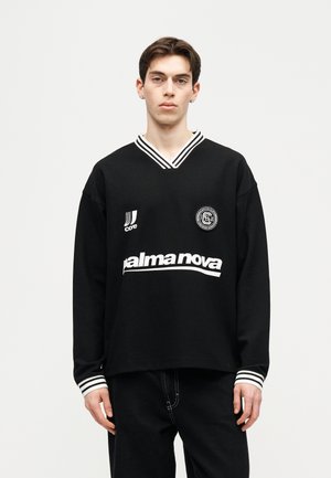 Young man wearing a black long-sleeve shirt with white stripes on collar and cuffs, featuring "palma nova" text and logo patches on front.