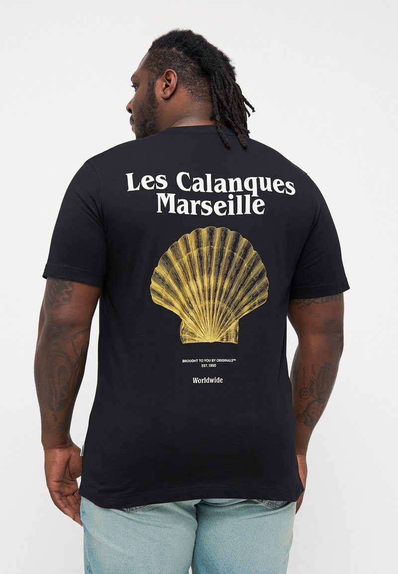 Schwarzes T-Shirt mit einem großen gelben Muscheldesign auf der Rückseite, mit dem Text "Les Calanques Marseille" darüber und zusätzlichem Branding darunter.