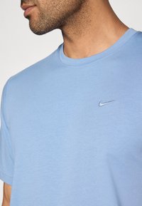 Φωτεινό μπλε βαμβακερό μπλουζάκι με στρογγυλή λαιμόκοψη, κοντά μανίκια και μικρό κεντημένο λογότυπο της Nike στο αριστερό στήθος. Λείος υφ ής.