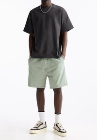 T-shirt noir à manches courtes, short vert menthe avec cordon de serrage, chaussettes blanches et baskets noires avec accents crème. Coupe simple et décontractée.