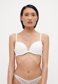 White padded bra with adjustable straps, featuring smooth fabric and a deep V-neckline. Paired with white sheer underwear with logos.