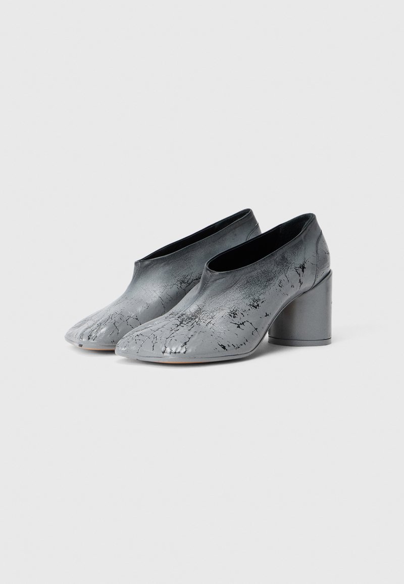 Une paire de bottines en cuir gris avec une texture marbrée noire et des talons cylindriques épais sur fond blanc.