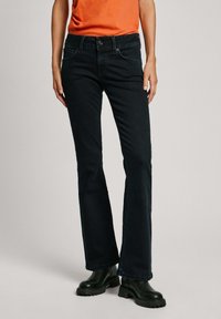 Zwarte, uitlopende jeans gemaakt van denim met voorzakken, riemlussen en een ritssluiting. Gestyled met een aansluitend oranje topje en zwarte chunky laarzen.