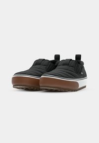 Sorte slip-on sko med quiltet overdel, elastiske sidepaneler, og en brun gummisåle med en hvit mellomsolestripe.