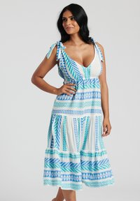 Blå och vit mönstrad klänning med djup V-ringning, knytband vid axlarna och en utsvängd nederkant med geometriska mönster. Lättviktig tyg.