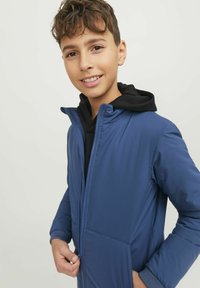 Blå vadderad jacka med svart huva, framzip, sidofickor, ribbade ärmar och en mjuk, lätt textur.