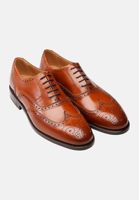 Scarpe brogue in pelle color cuoio con design a punta d'ala, perforazioni decorative e lacci marroni. Finitura lucida con suola resistente.