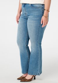 Jean en denim bleu évasés avec une taille ajustée, design à cinq poches et délavage clair. L'ourlet est brut, associé à des talons imprimés léopard.