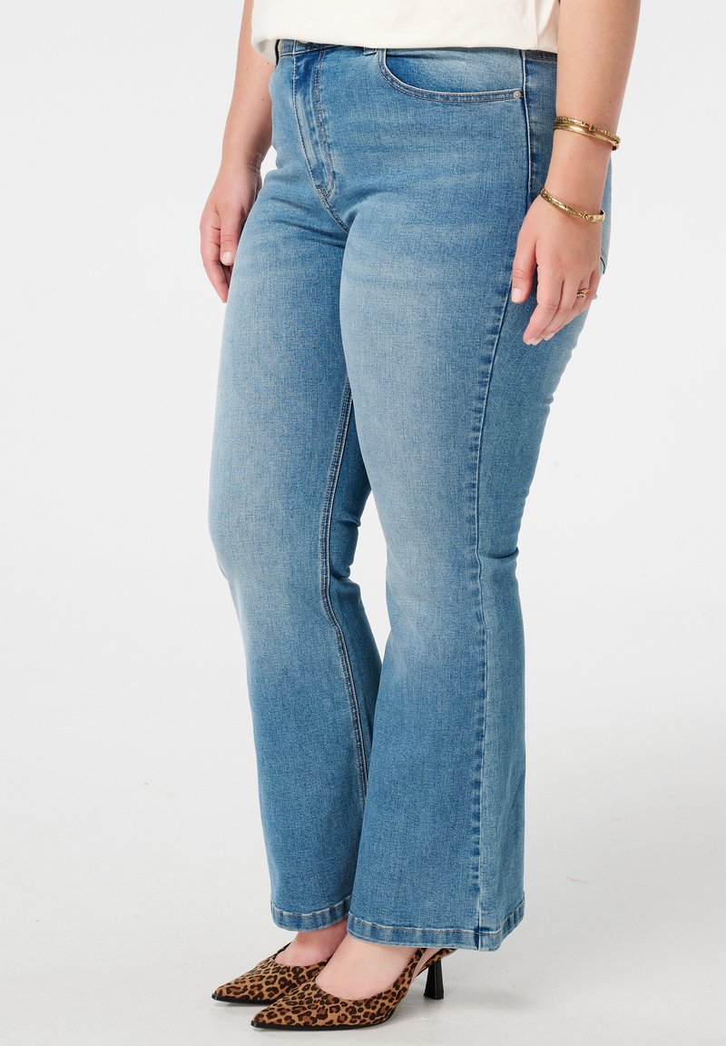 Jean en denim bleu évasés avec une taille ajustée, design à cinq poches et délavage clair. L'ourlet est brut, associé à des talons imprimés léopard.