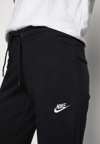 Svarta sweatpants i bomullsblandning, med elastisk midja och dragsko samt en vit broderad Nike-logga på låret.