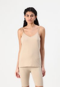 Beez, ilma varrukat tank top v-kaelusega, valmistatud pehmest kangast. Lihtne ja keha lähedane lõige, mida täiustavad sobivad lühikesed püksid.