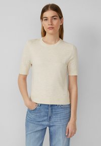 Bež neelate shirt, lühikeste varrukatega, ümarate kaelustega, sileda tekstuuriga ja õrna brändi sildiga alläärs. Koos helesiniste teksadega.