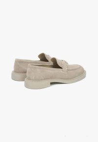 Beige suede loafers with a rounded toe, detailed stitching, and slip-on design. Features a textured sole and subtle logo accents.