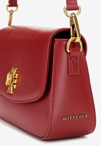 Rode leren schoudertas met een magnetische flap, gouden hardware, gebosseleerde merknaam en een gestructureerde vorm. Voorzien van een afneembare schouderband.