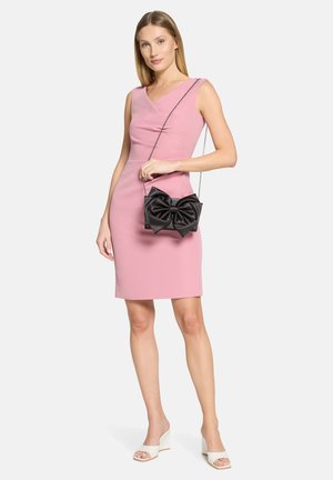 Robe rose ajustée avec un décolleté en V, accompagnée d'un sac en satin noir orné d'un grand nœud, et de sandales compensées blanches.