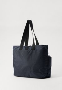Sac fourre-tout bleu marine en tissu durable, avec des poignées noires, une poche zippée et une forme structurée et rectangulaire.
