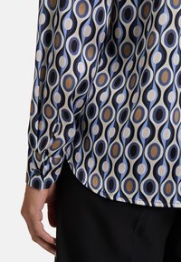 Camicia a maniche lunghe in tessuto morbido con un motivo astratto di ovali nei toni del blu, nero e oro; dettagli ai polsini con bottone.