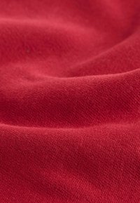 Tessuto rosso con una superficie morbida e testurizzata e schemi di tessitura sottili, disposto in pieghe dolci e fluenti.