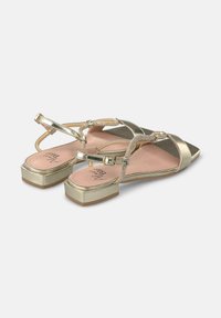 Scarpe piatte in metallo dorato con punta affusolata, cinturini regolabili e tacchi spessi. Texture liscia con una soletta rosa e dettagli aggiuntivi sui cinturini.