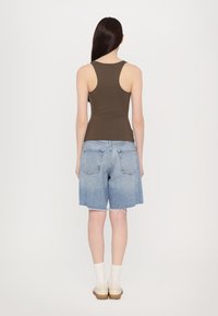 Top a canotta marrone e pantaloni shorts in denim blu chiaro con orlo sfilacciato. Modello che indossa calzini bianchi e scarpe beige, visto da dietro.