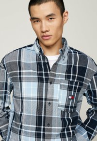 Camisa de cuadros abotonada en colores azul, marino y gris. Presenta un bolsillo en el pecho con un logo y un cuello clásico. Tejido de algodón, patrón de cuadros.