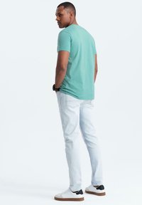 Světle zelené tričko s krátkým rukávem a kulatým výstřihem, spárované se světle modrými džíny a bílými teniskami se černými akcenty.