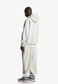 Light gray, oversized hoodie with a hood, paired with loose-fitting sweatpants. Rubber-soled athletic shoes with a gray and red design.