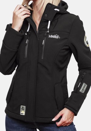 Frau trägt schwarze Softshelljacke mit Kapuze, Reißverschlusstaschen und Berg-Logo, richtet mit einer Hand den Kragen.