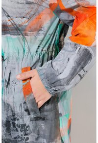 Multikleurenjack met abstracte patronen in grijs, oranje en teal, voorzien van elastische manchetten en een zak aan de linkerkant.