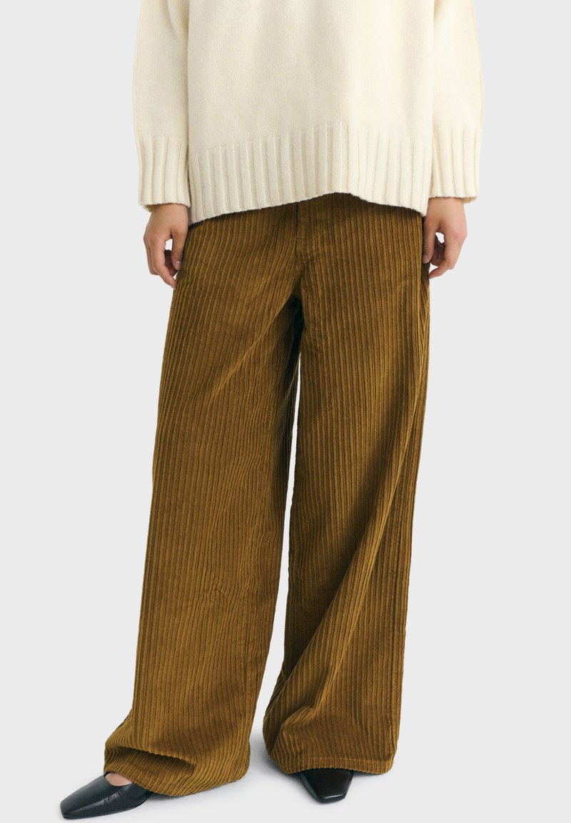 Wide-leg brown corduroy pants worn with black square-toe shoes and an off-white ribbed sweater.