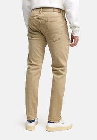 Vaqueros de mezclilla beige con un corte ajustado, que cuentan con bolsillos traseros y una etiqueta marrón en la cinturilla. Combinados con zapatillas blancas.
