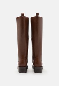 Braune Leder-Stiefel bis zum Knie mit glatter Textur, Seitenzippern und gestapeltem Gummihilfsabsatz. Schlaufe oben für ein einfaches Anziehen.