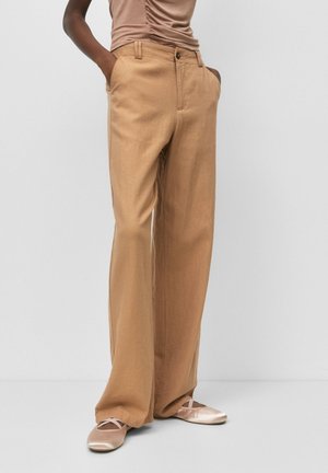 Beige wide-leg linen trousers with front pockets and a button closure, complemented by light pink ballet flats with crisscross straps.