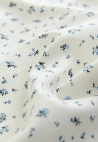Tessuto di cotone con sfondo bianco, caratterizzato da piccoli fiori blu e accenti neri in un motivo sparso, superficie testurizzata.