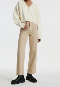 Vit kortärmad tröja med stora knappar, kombinerad med beige högmidjade vida jeans och svarta kraftiga ankelstövlar.