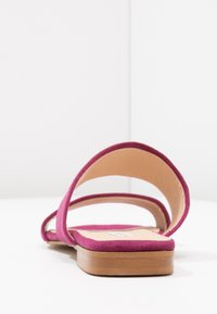 Ploché sandály s dvojitými širokými růžovými semišovými pásky a béžovou vycpanou stélkou na dřevěné podrážce, zobrazené z zadního úhlu.
